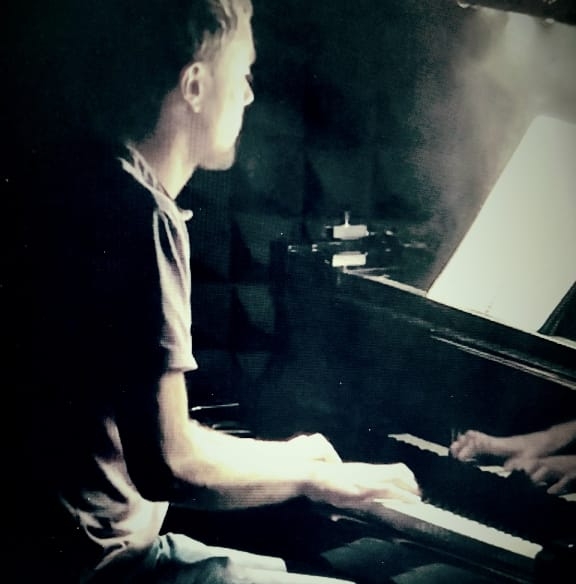 Austin Kimble playing an acoustic piano, with his hands reflected in the instrument
